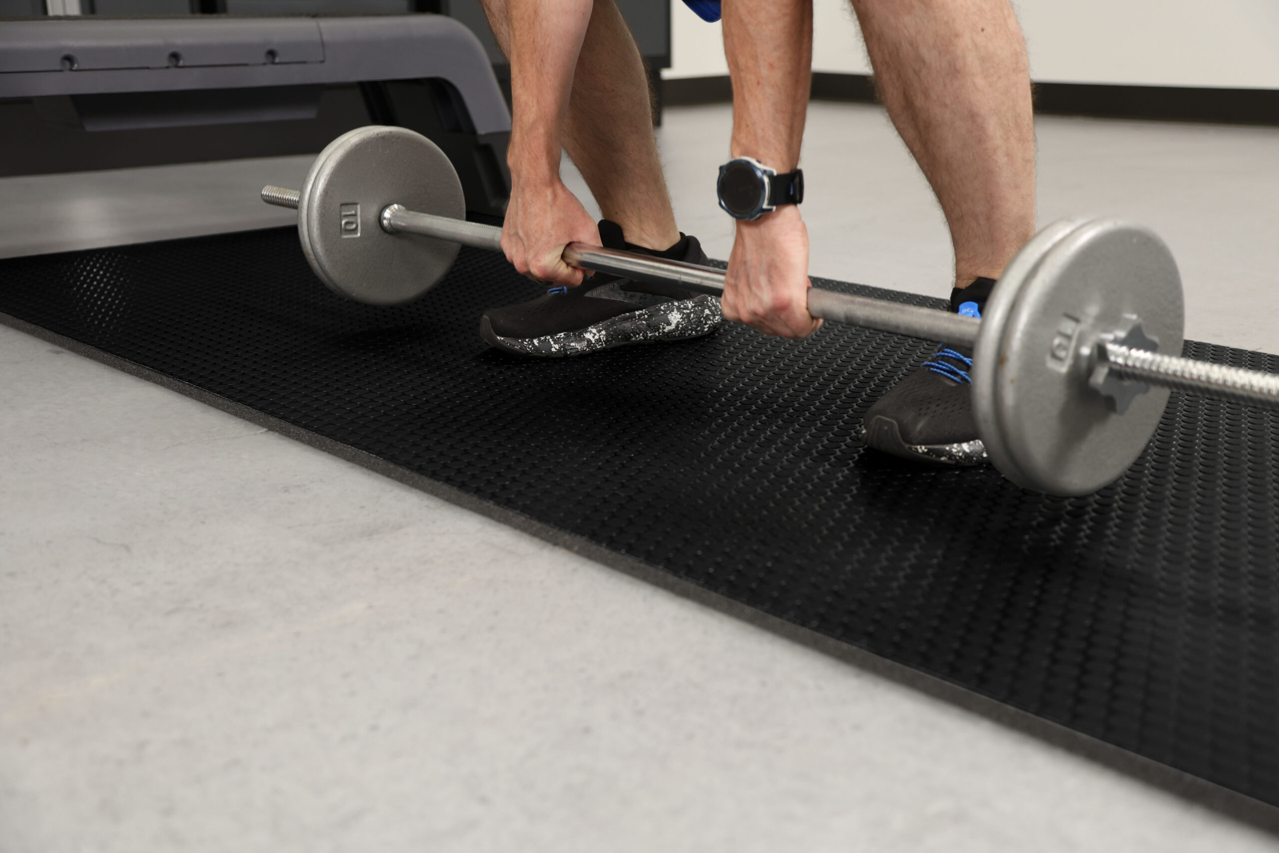 Person lifting a barbell on a black cushioned gym flooring mat