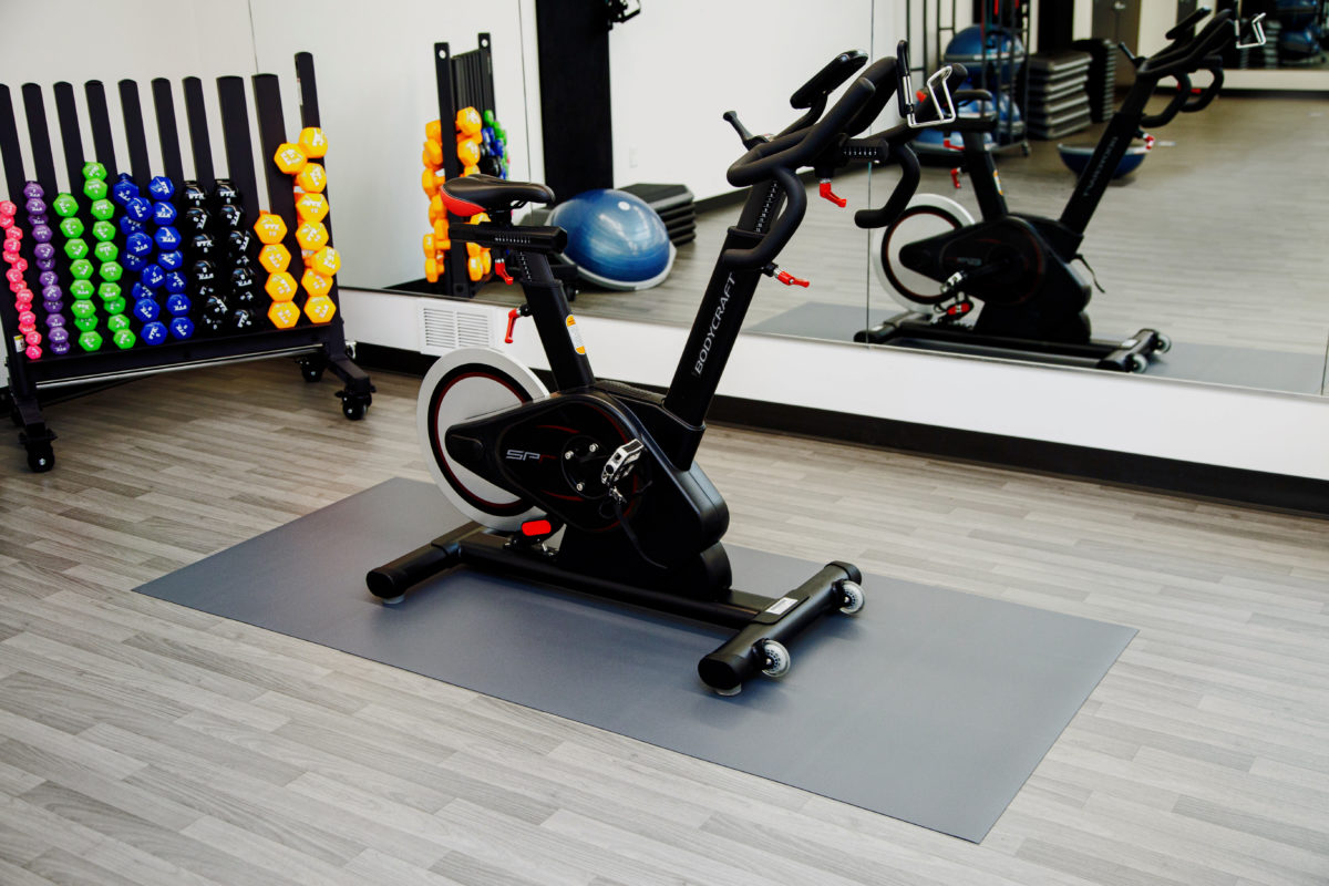 Stationary exercise bike on a gray protective equipment mat in a fitness studio